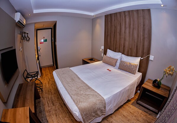 Une chambre d’hôtel moderne avec un grand lit, une tête de lit en bois, des tables de chevet, une télévision et un bureau.