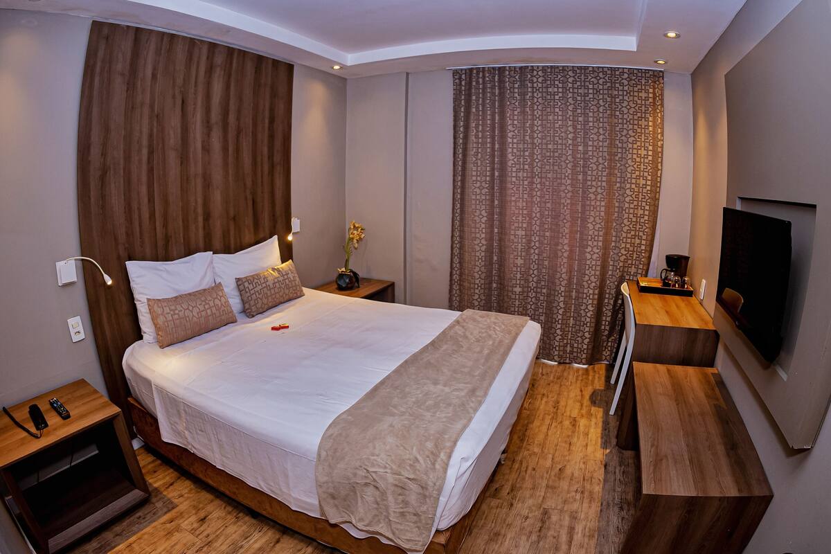 Ein modernes Hotelzimmer mit einem großen Bett, einem Holzkopfende, einem Flachbildfernseher und einem kleinen Nachttisch.