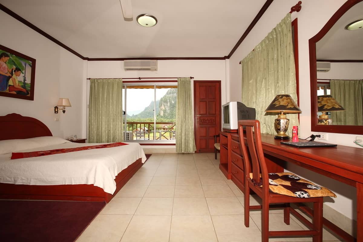 Habitación de hotel con cama, escritorio, silla y balcón con vista a la montaña.
