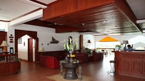A spacious lobby with a high ceiling, wooden paneling, a reception desk, and a seating area with a coffee table and chairs. - Vansana Vang Vieng (Vang Vieng)
