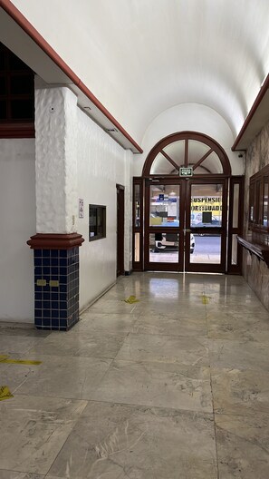 A spacious hallway with a tiled floor, a large arched doorway, and a trash bin.