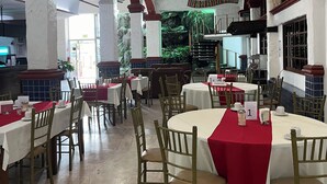 A restaurant with round tables, red tablecloths, and wooden chairs.