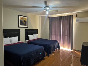 A hotel room with two beds, a ceiling fan, a framed picture on the wall, and a window with curtains.
