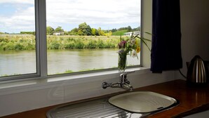 A kitchen with a window view of a river, a sink, and a vase with flowers. - Whanganui River Top 10 Holiday Park (Whanganui)