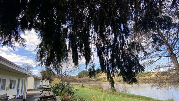A lakeside property with a wooden deck, picnic tables, and a grassy lawn. - Whanganui River Top 10 Holiday Park (Whanganui)