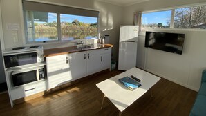 A compact kitchen with a view of a lake, a microwave, a refrigerator, and a dining table with a book and remote control. - Whanganui River Top 10 Holiday Park (Whanganui)