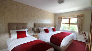 A hotel room with two beds, a window with curtains, and a patterned wallpaper.