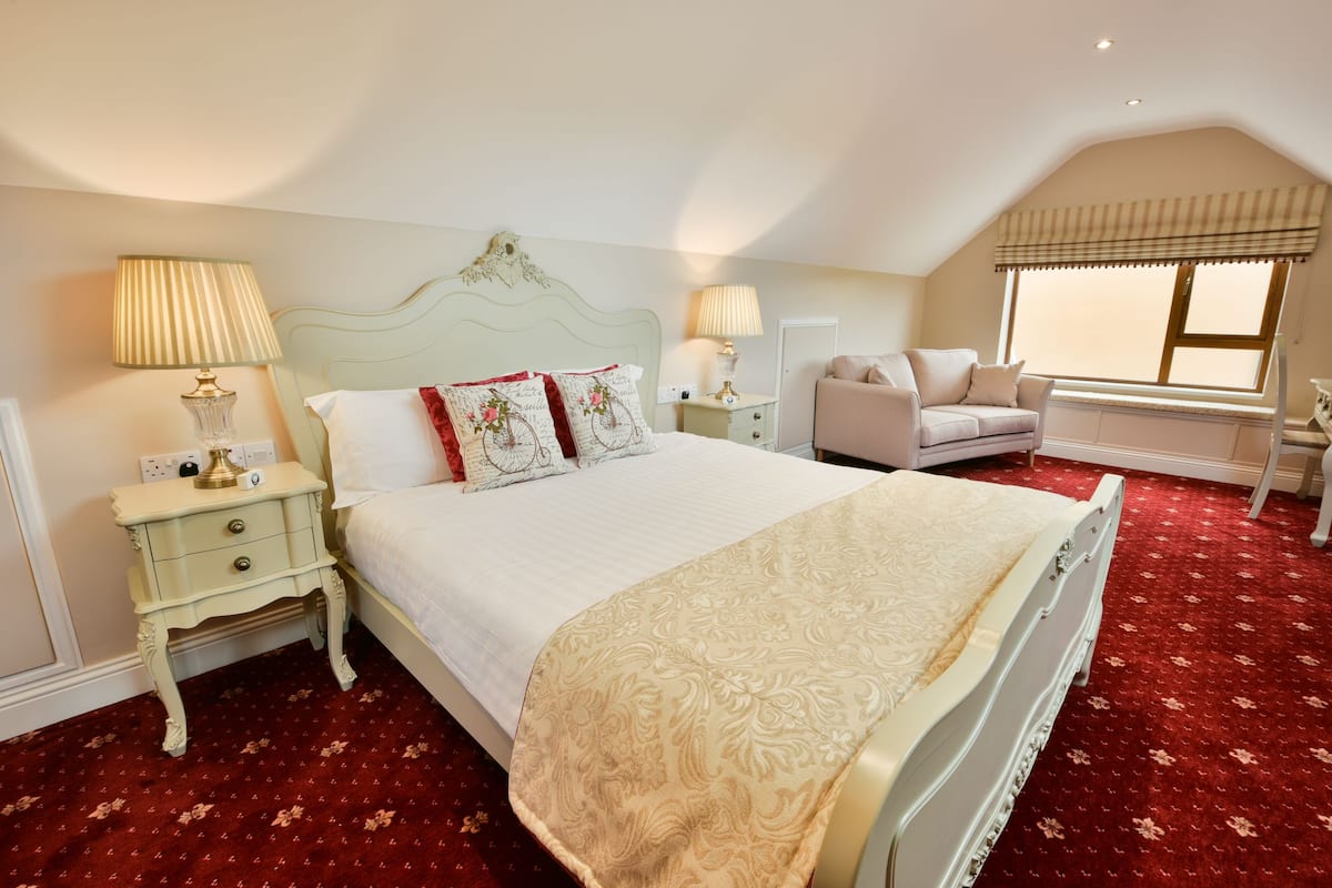 Ein Schlafzimmer mit einem großen Bett, zwei Nachttischen, einem kleinen Tisch, einem Sessel und einem Fenster mit Blick.