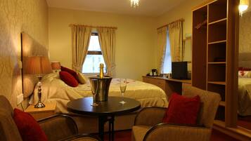 A hotel room with a bed, a desk, a chair, a table with a bottle and glass, a TV, and a wardrobe.