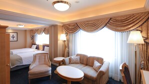 Una habitación de hotel con cama, sofá, sillón, una mesita y una lámpara.