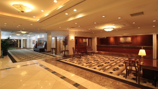 Un vestíbulo de hotel con piso de mármol, un mostrador de recepción y varias zonas de estar.