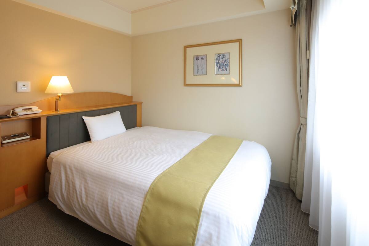 Une chambre d’hôtel avec un lit, une table de chevet avec une lampe, un téléphone et un tableau encadré au mur.