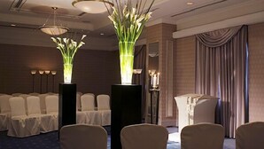 Un salón de conferencias con filas de sillas, un atril y dos arreglos florales iluminados.