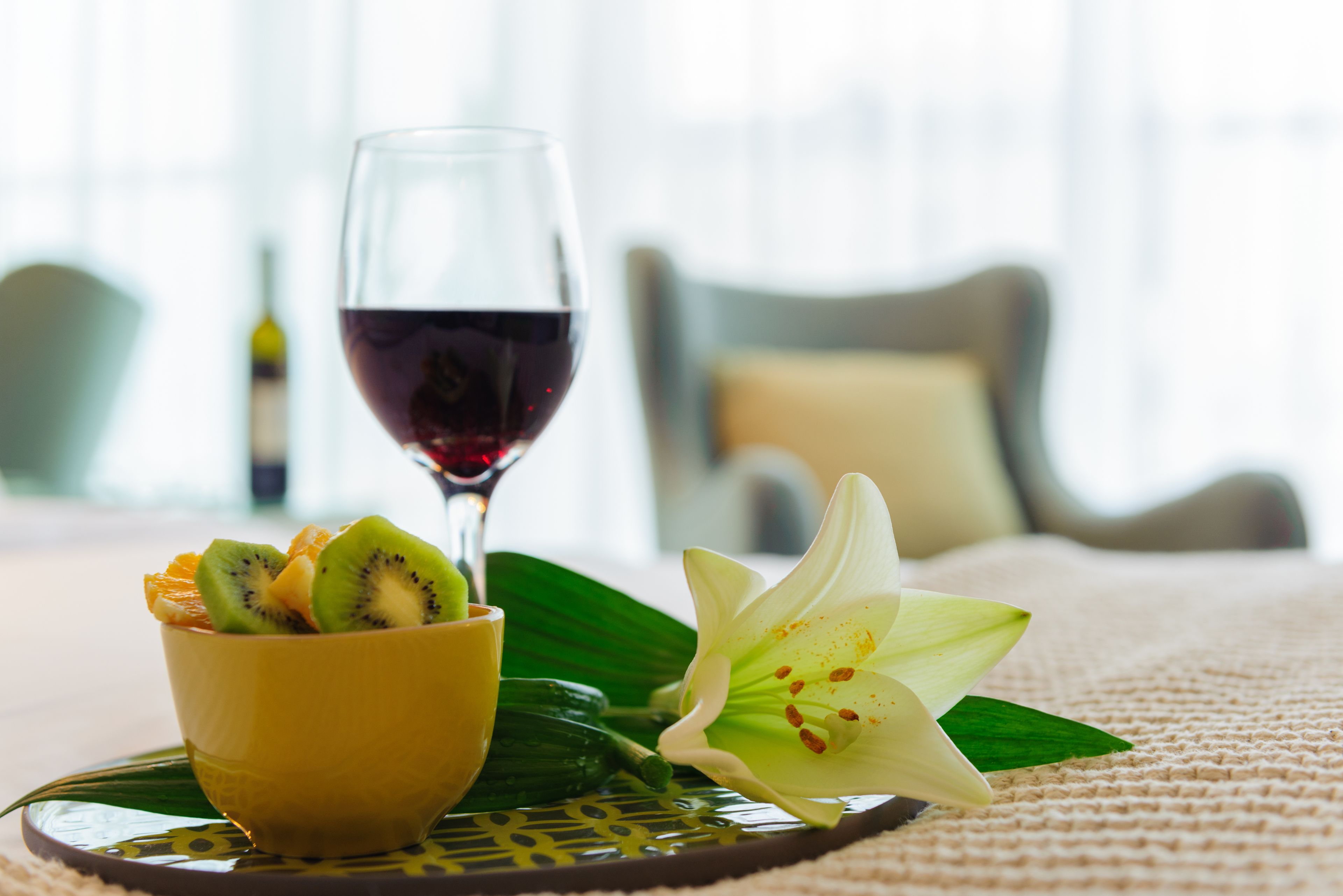 A bowl of fruit and a glass of red wine on a table with a white flower.