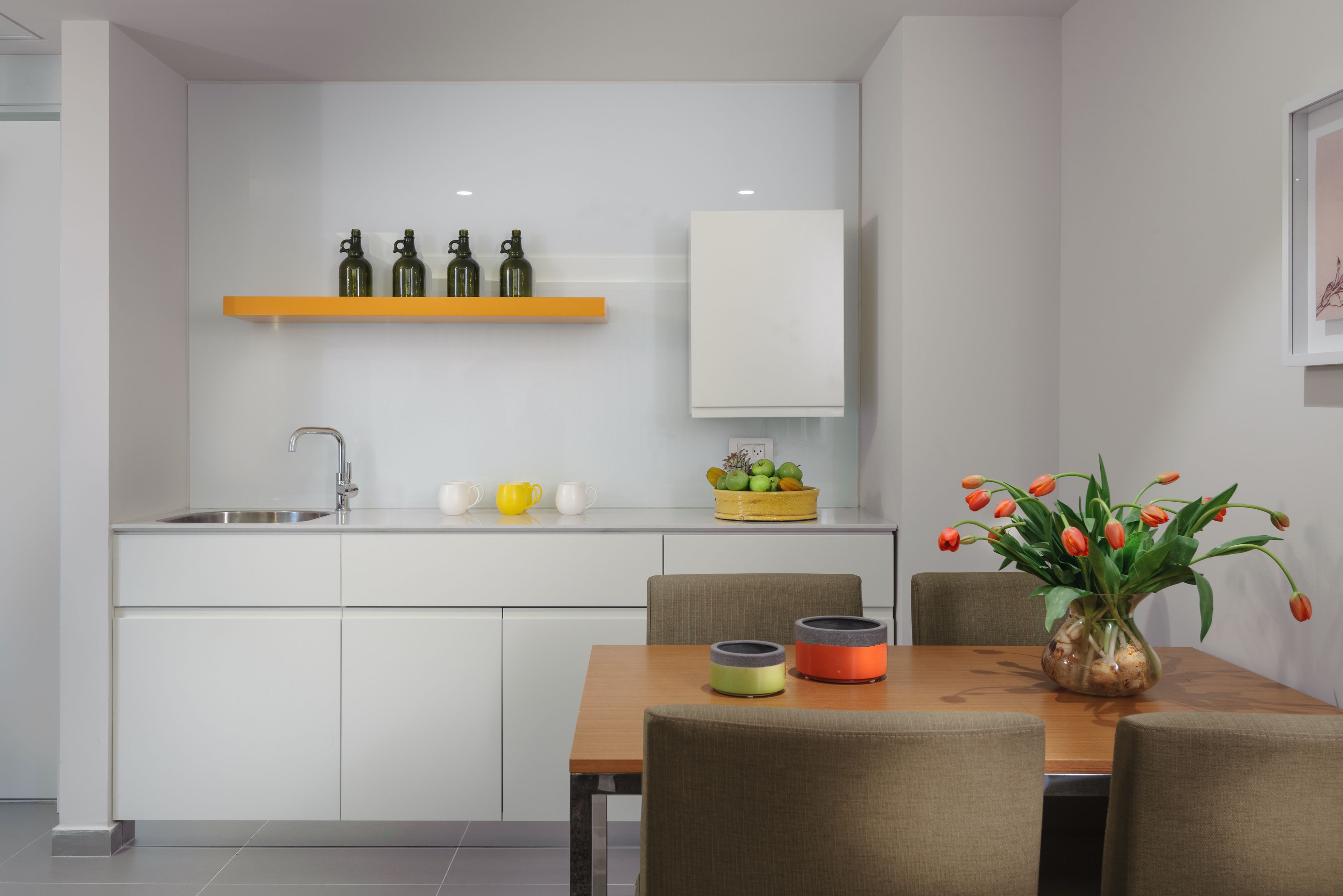 Una cocina compacta con un lavamanos integrado, una mesa de madera con sillas, y un jarrón de tulipanes sobre la mesa.