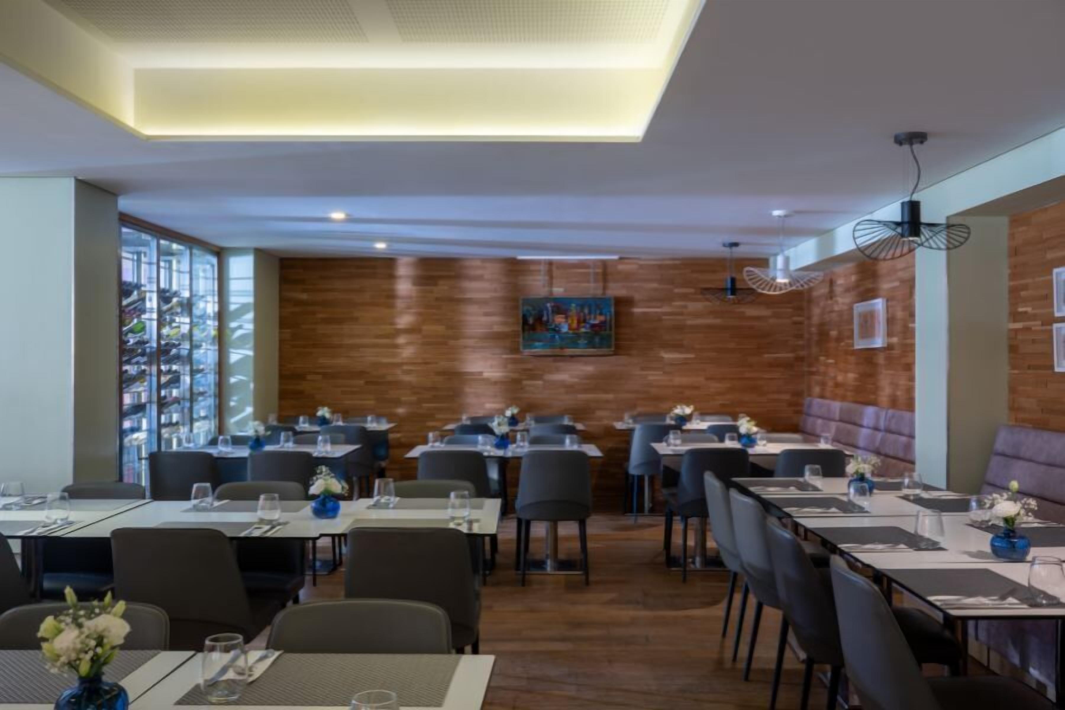 A modern restaurant with multiple tables and chairs, a wooden wall, and a ceiling with recessed lighting.
