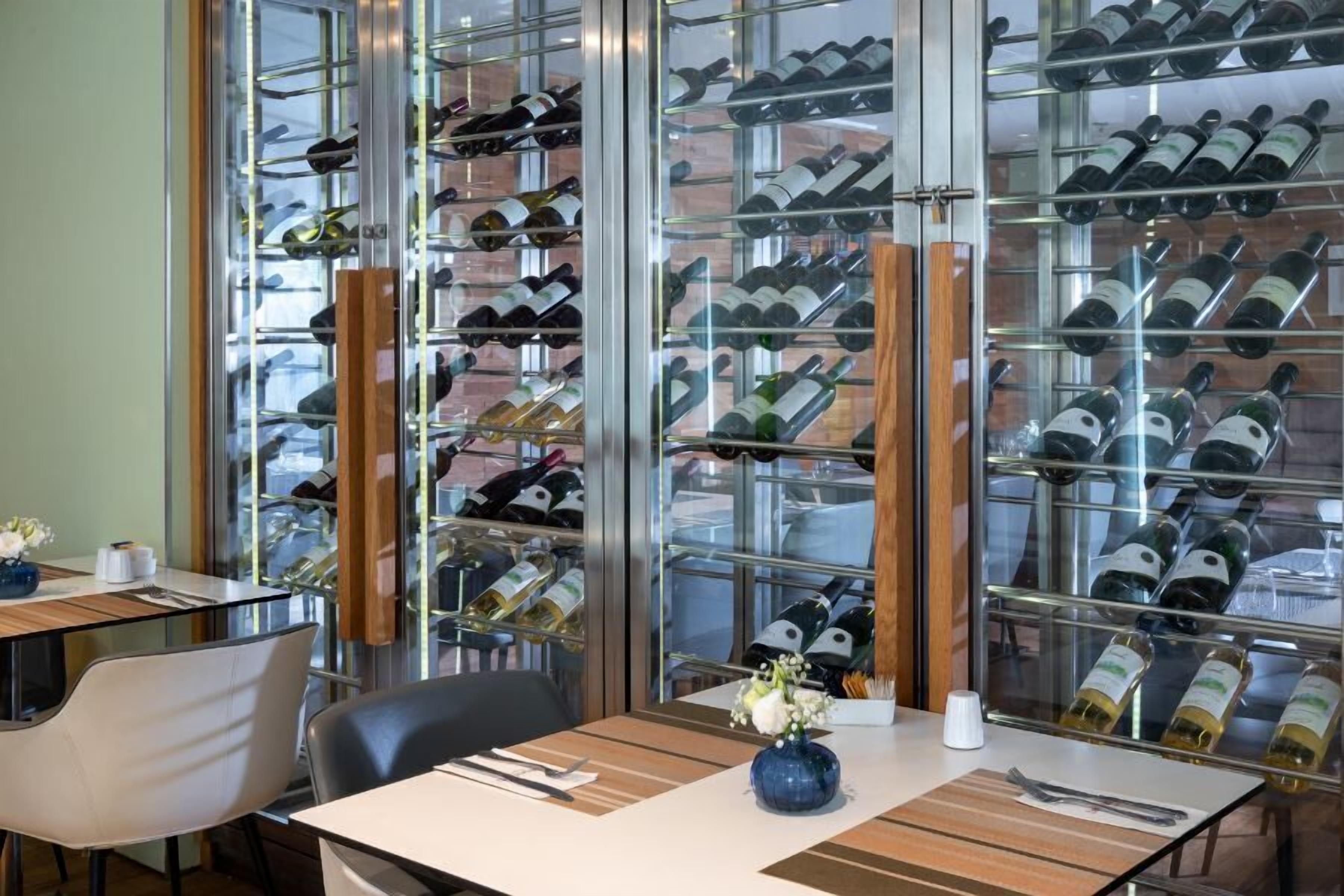 A restaurant with a wine rack filled with various bottles, a table with a vase of flowers, and a chair.