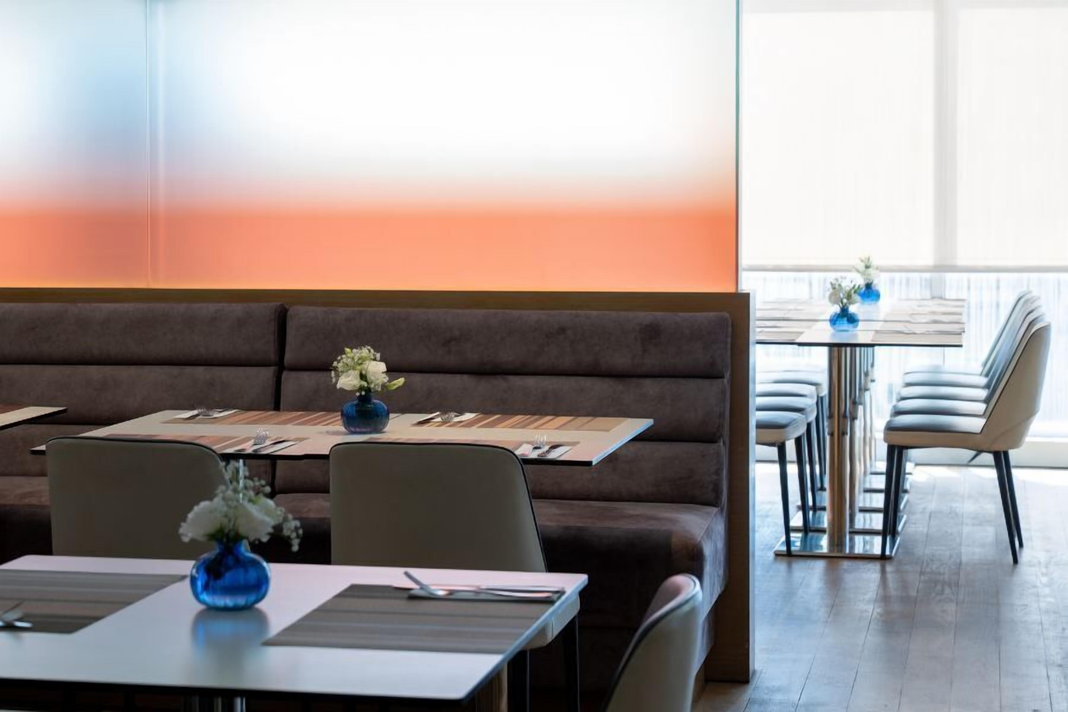 A restaurant with a long brown sofa, tables with blue vases, and a bright window view.