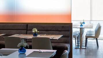 Un restaurante con un sofá marrón largo, mesas con jarrones azules y una vista luminosa a través de la ventana.