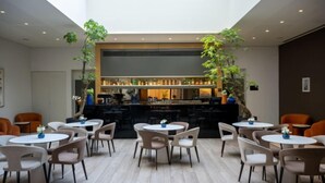 Un comedor interior moderno con mesas y sillas redondas, una barra al fondo y plantas de interior.
