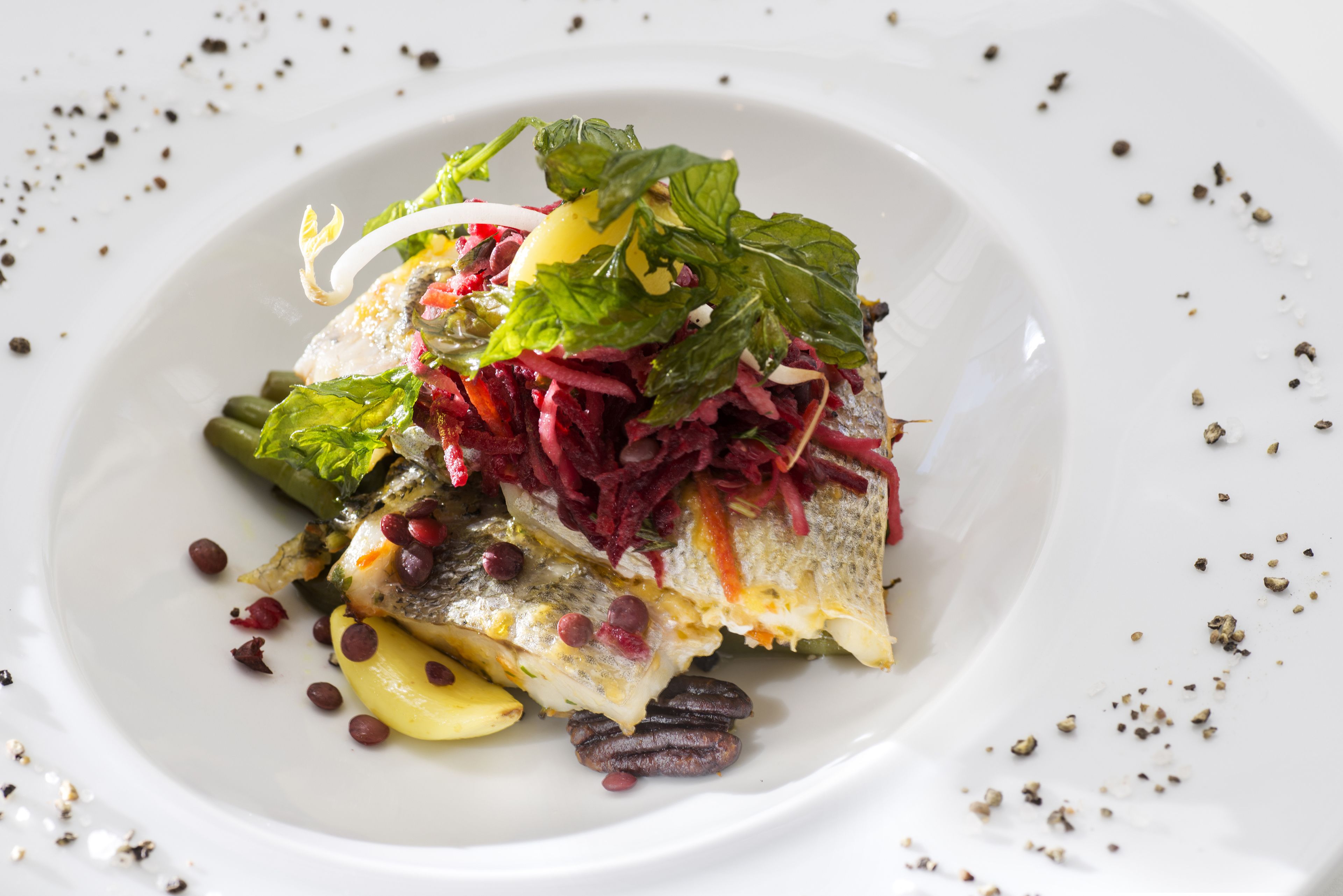 Un plato blanco con un filete de pescado, verduras verdes y remolacha roja.