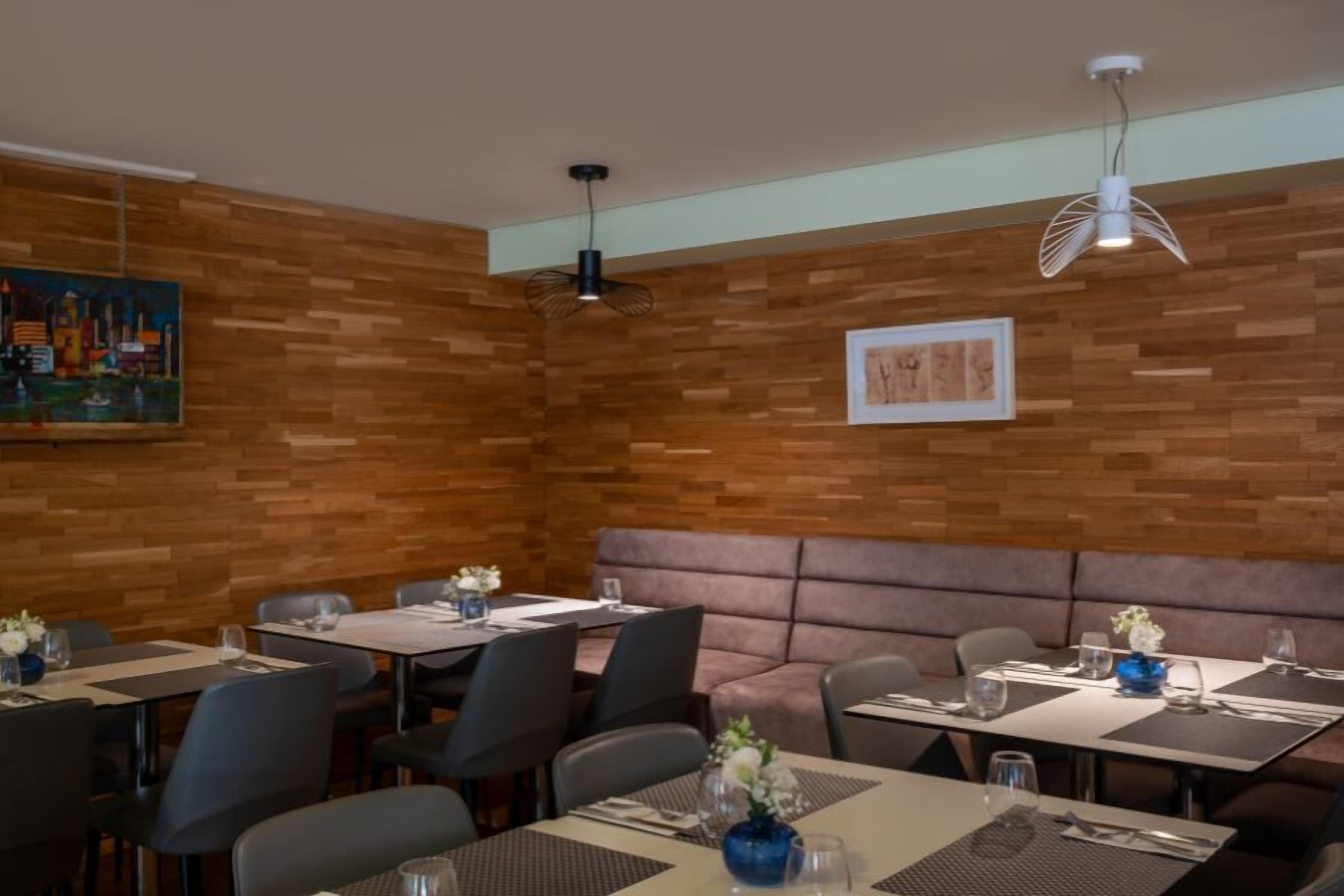 A restaurant with wooden walls, black and grey chairs, and tables set with placemats and glasses.