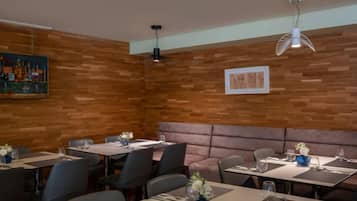 Un restaurante con paredes de madera, sillas negras y grises, y mesas dispuestas con manteles individuales y vasos.