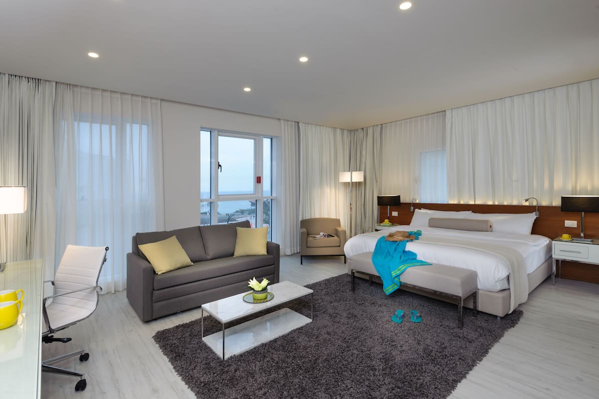 A hotel room with a bed, a sofa, a chair, a coffee table, and a window.