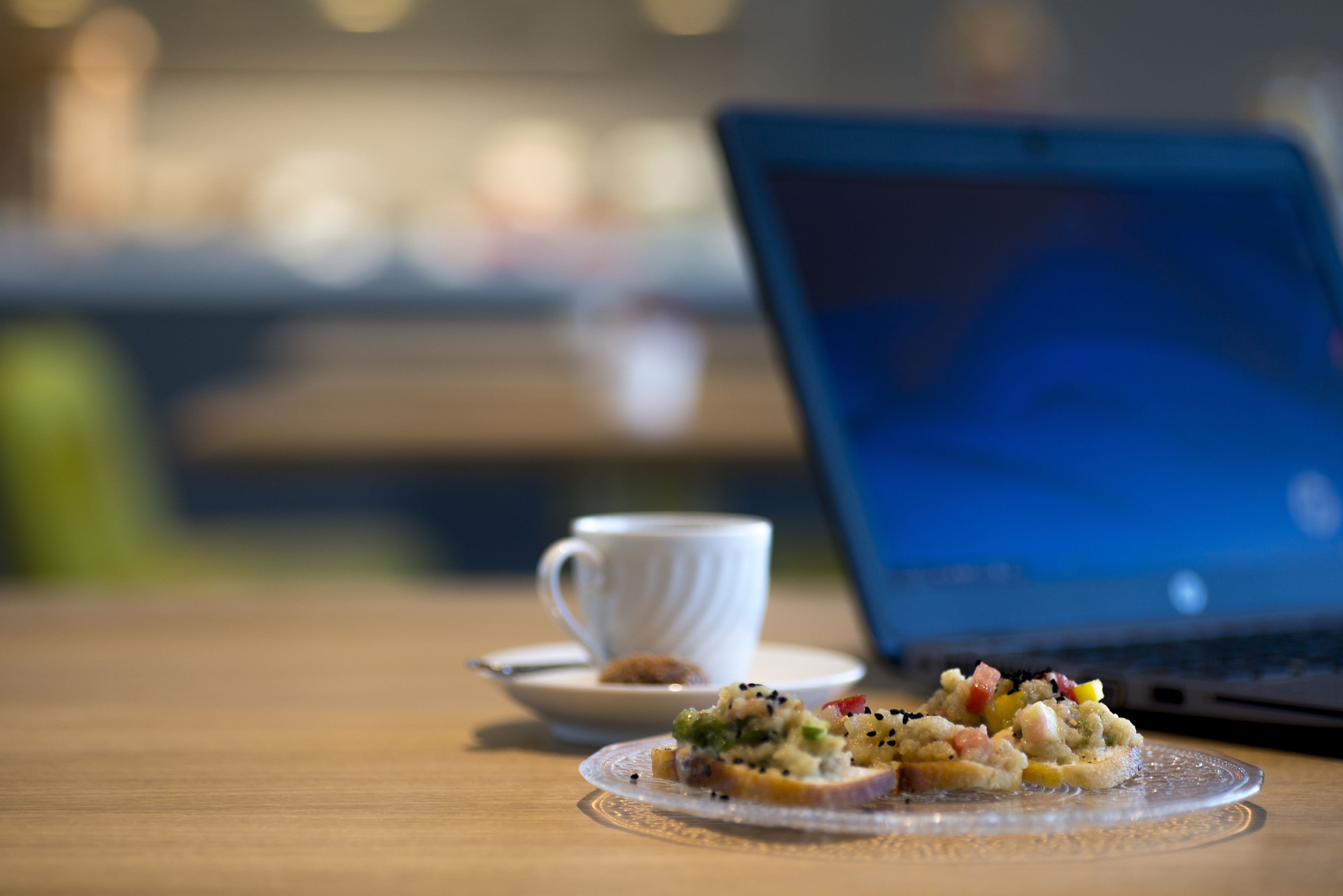 Um laptop sobre uma mesa, com uma chávena e um prato de comida.
