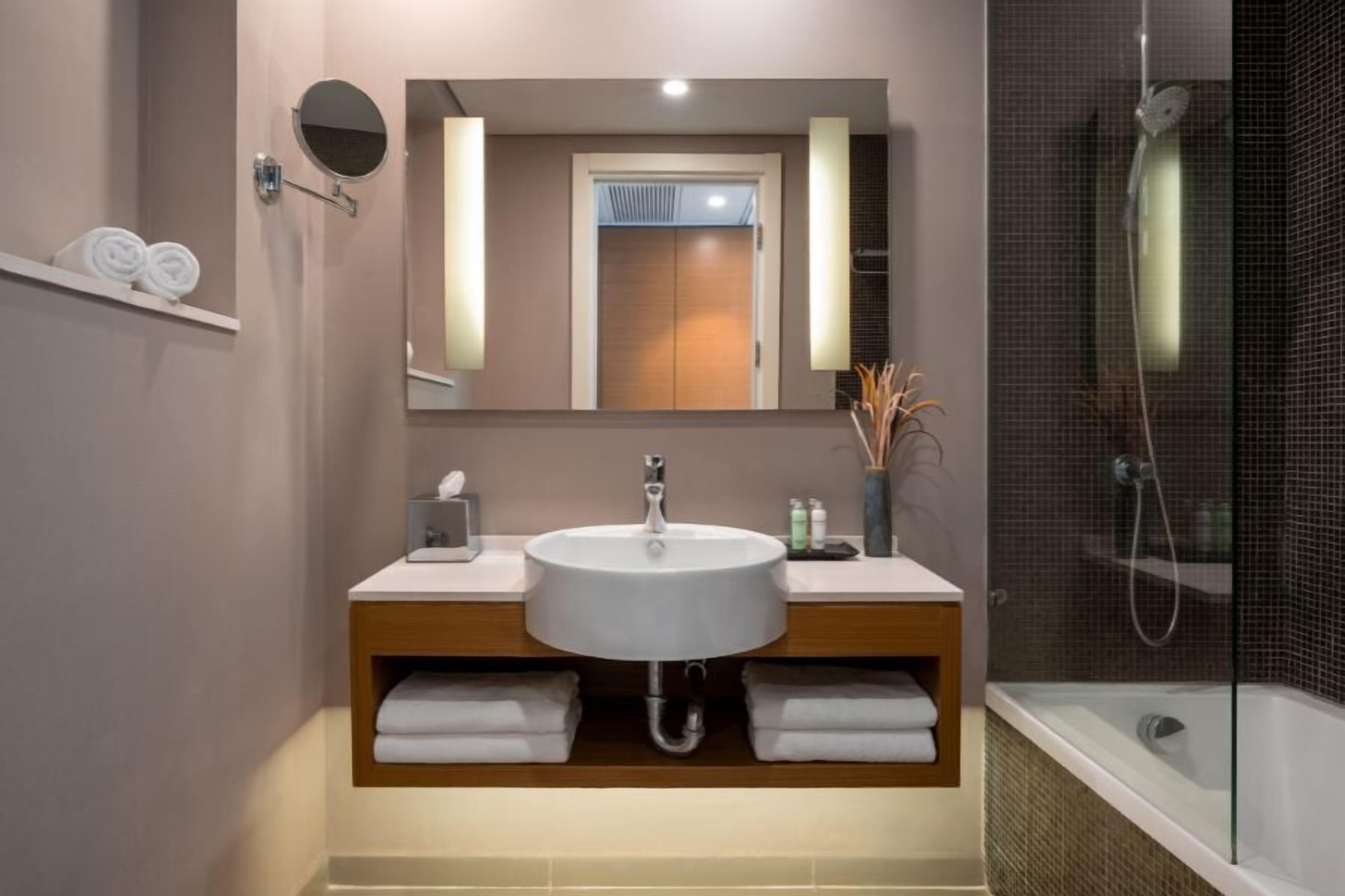 Un baño moderno con lavamanos, espejo, toallero y ducha.