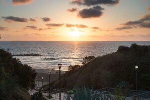 Vista al atardecer sobre el océano, con una playa y escaleras que bajan hacia el agua.