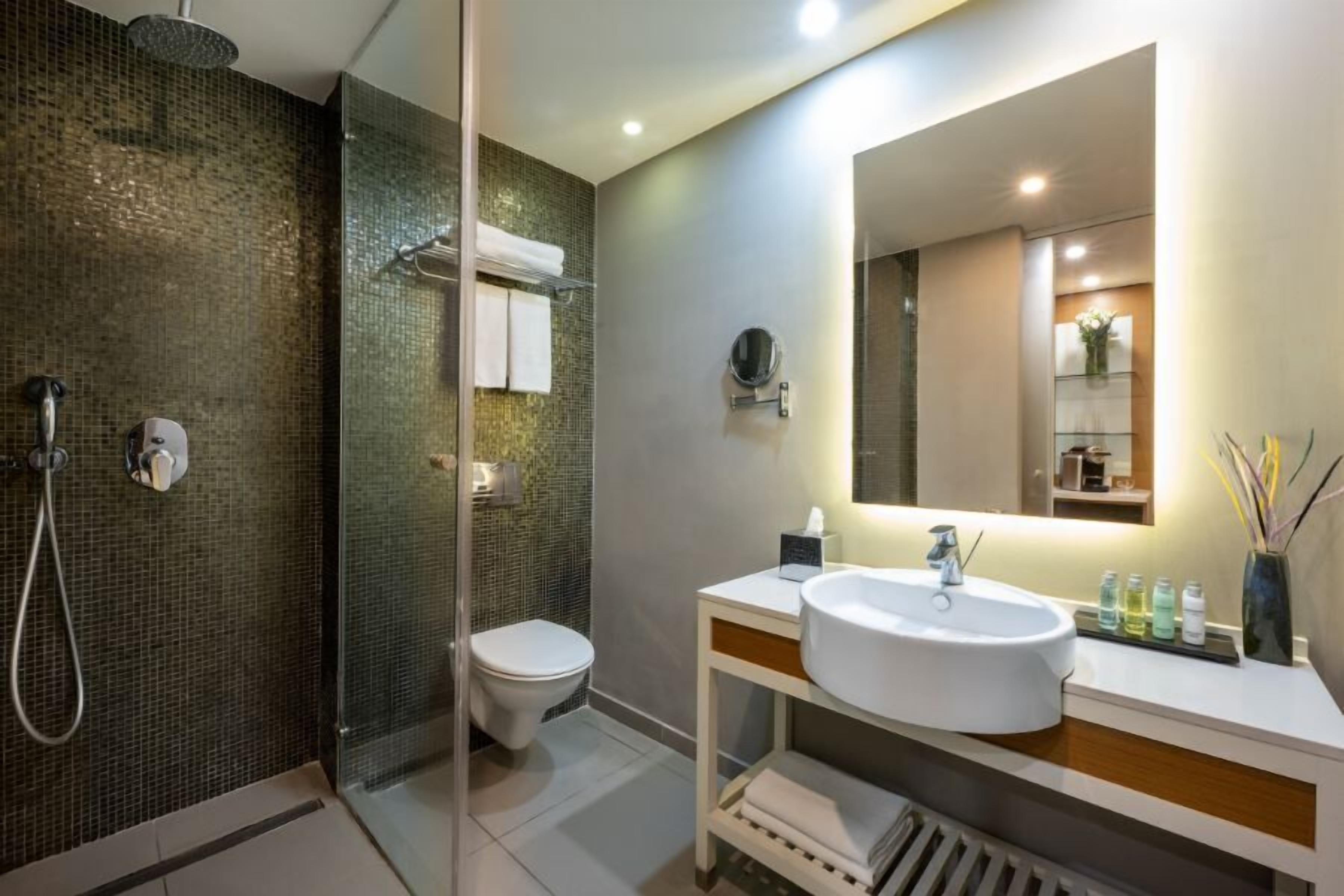 Un baño moderno con ducha de vidrio, inodoro, lavamanos con espejo y perchero para toallas.