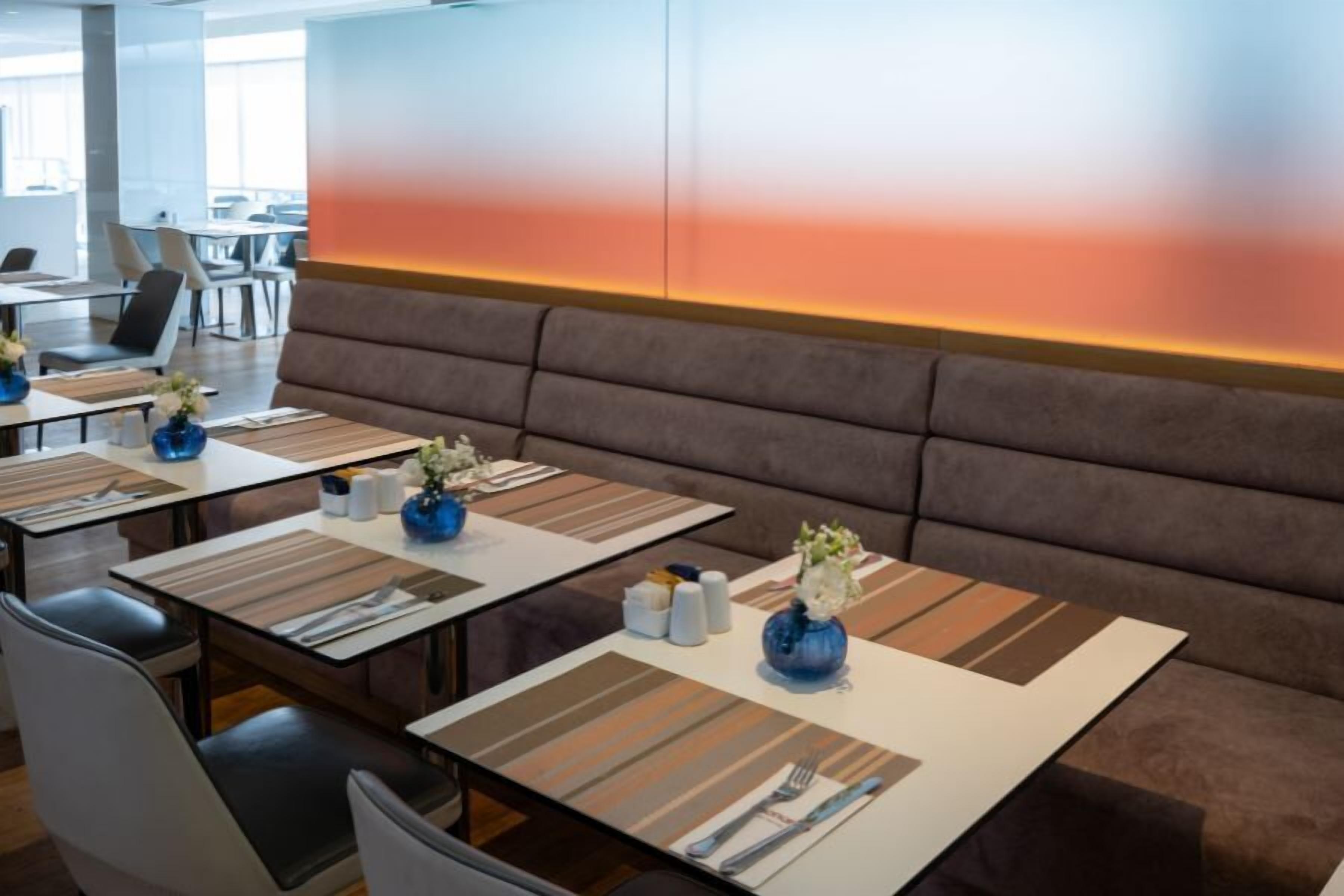 Un espace de restauration moderne, doté de banquettes et de tables, chacune agrémentée de couverts et de vases décoratifs.