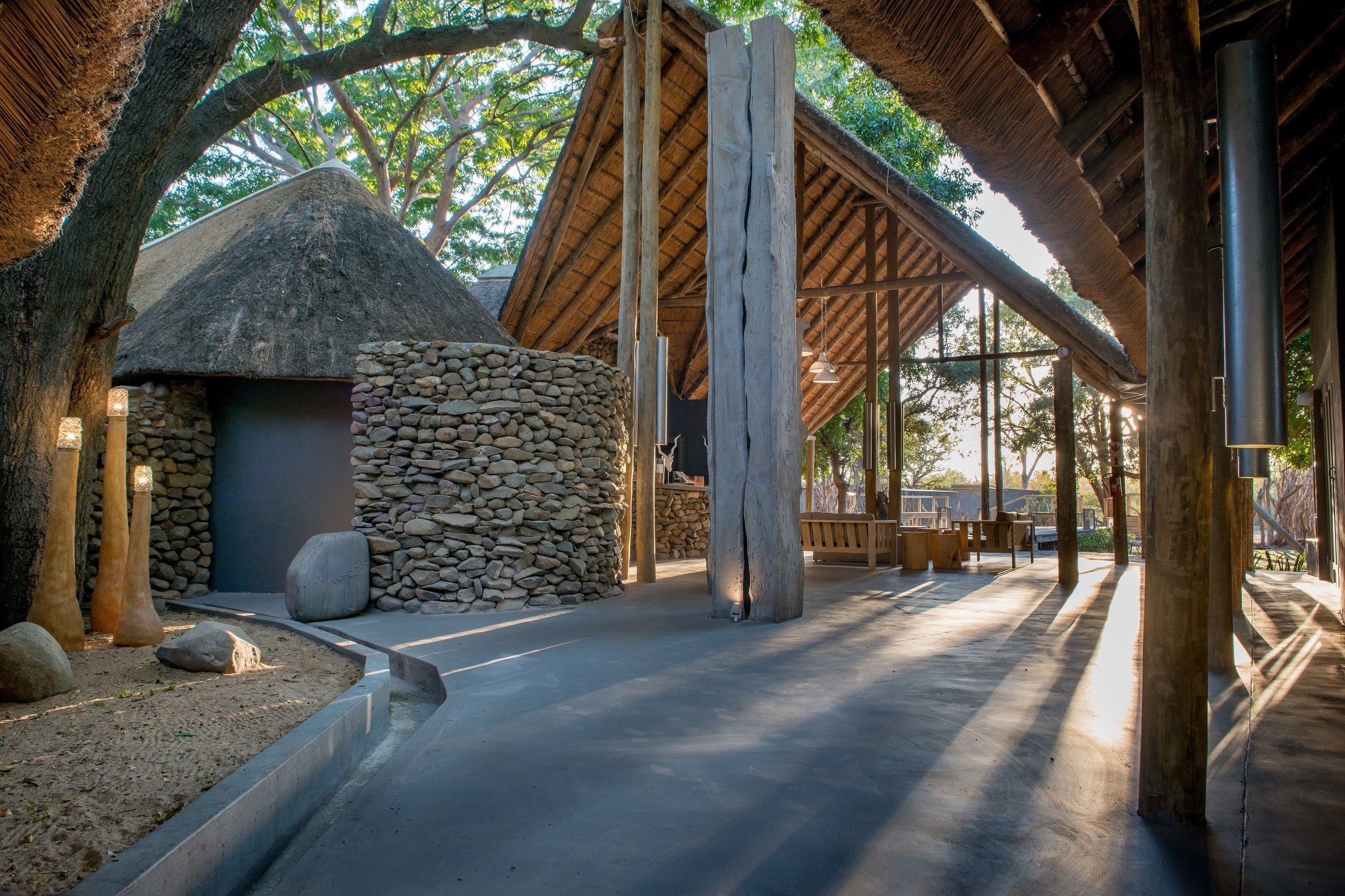 Una cabaña con techo de paja, pared de piedra, vigas de madera y un camino de concreto.