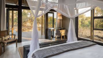 A bedroom with a large bed, a desk, and a chair, all in a modern, open design with large windows.