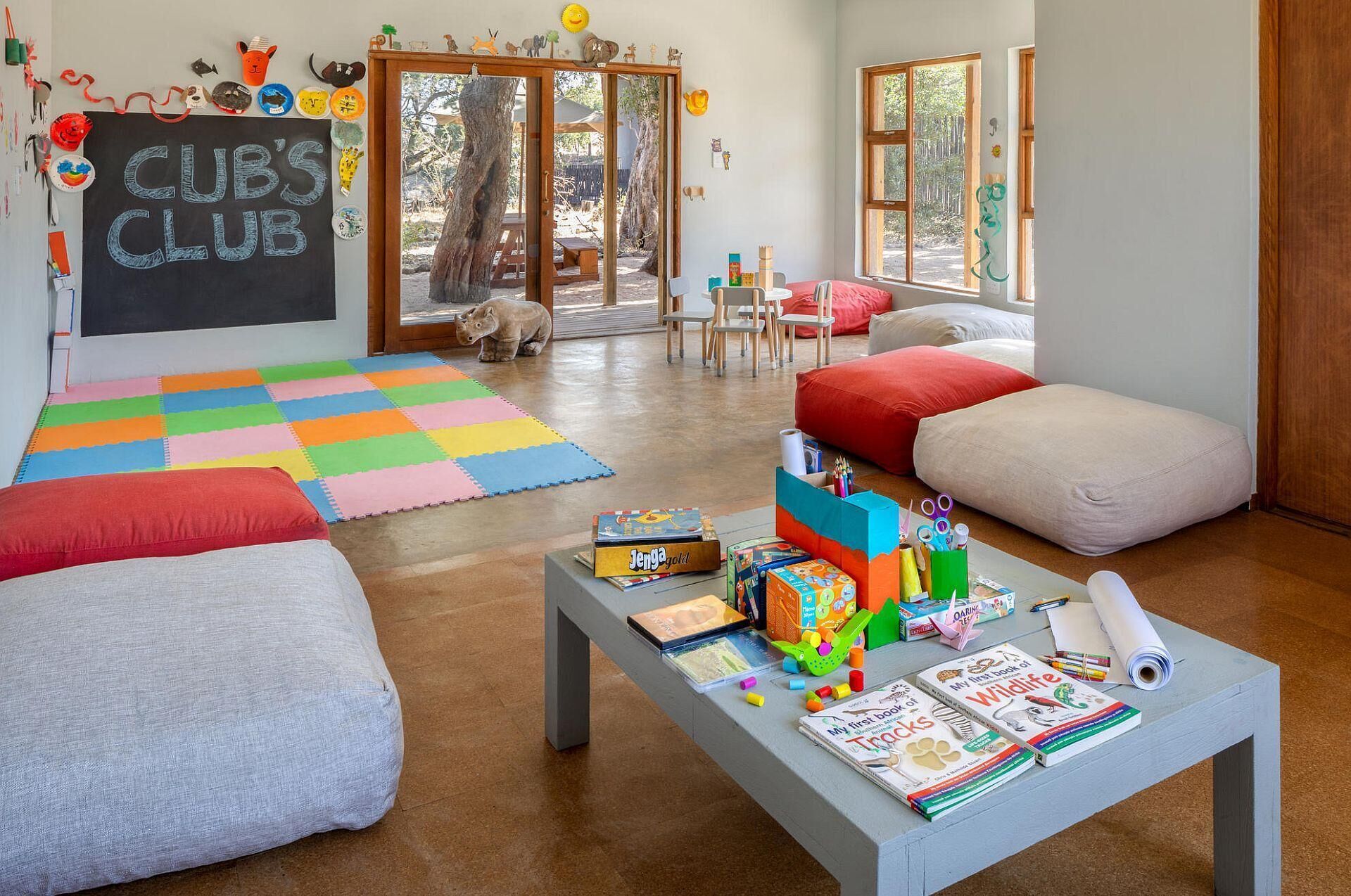 Ein gemütlicher Kinderraum mit einer bunten Spielmatte, einer Couch und einem Tisch mit Büchern und Spielzeug.