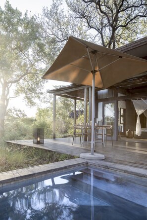 A pool area with a pergola, outdoor furniture, and a view of trees.