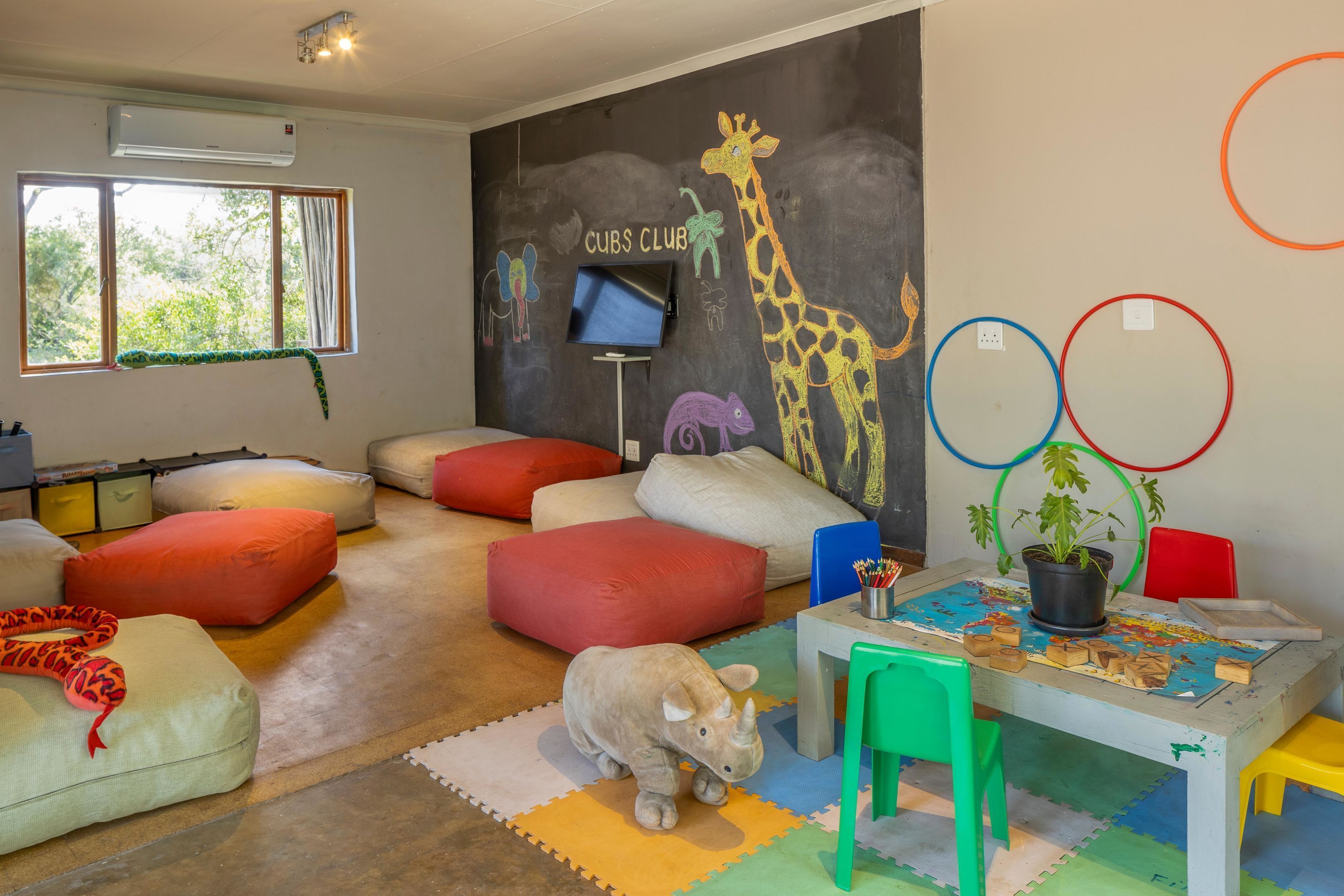 A children's playroom with a mural, a television, and colorful seating.