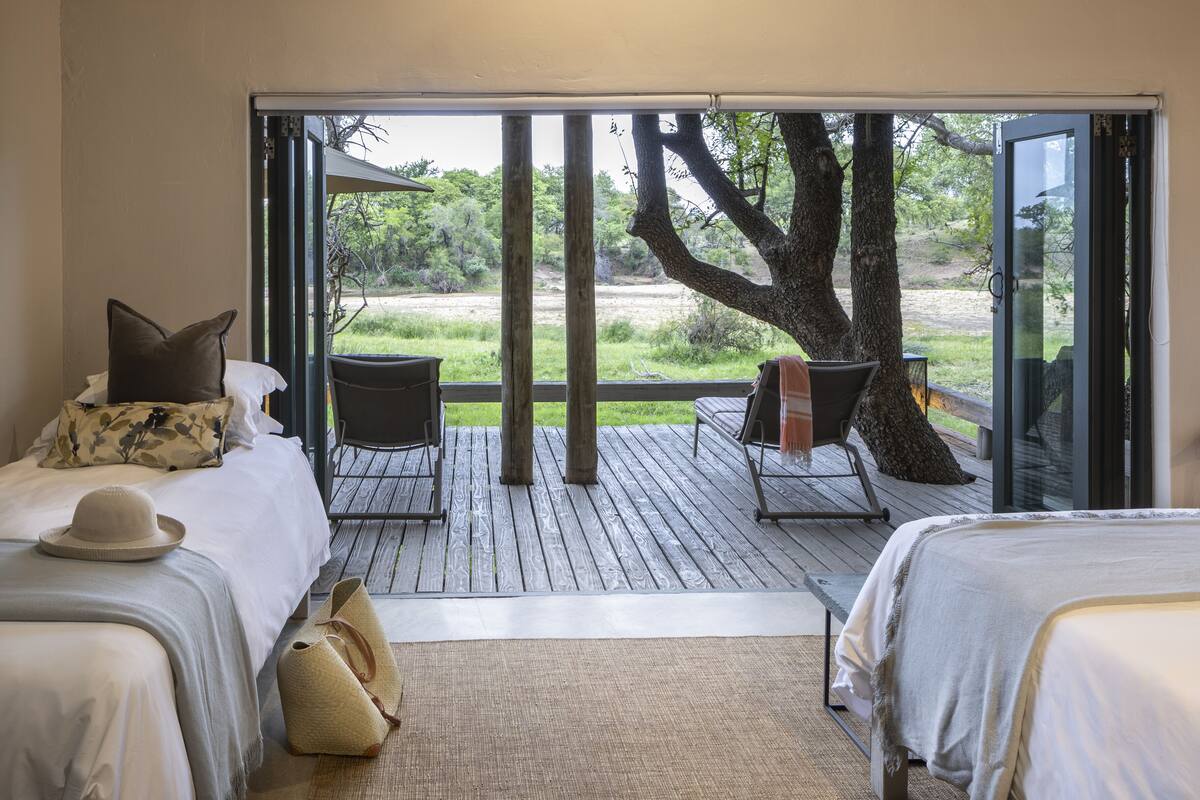 A bedroom with two beds, a large window, and a view of a tree and landscape.