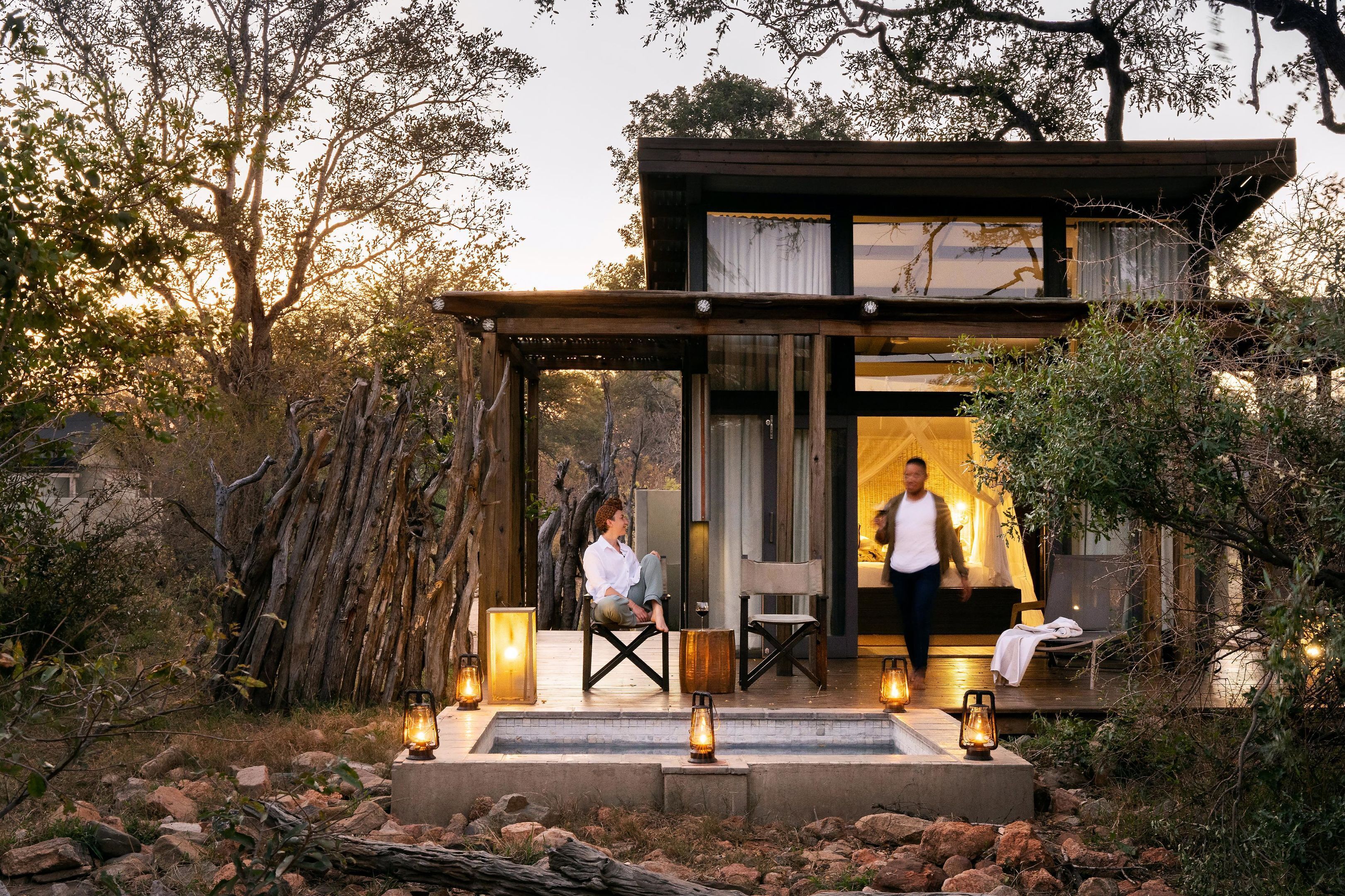A modern outdoor structure with a wooden deck, seating, and lanterns.