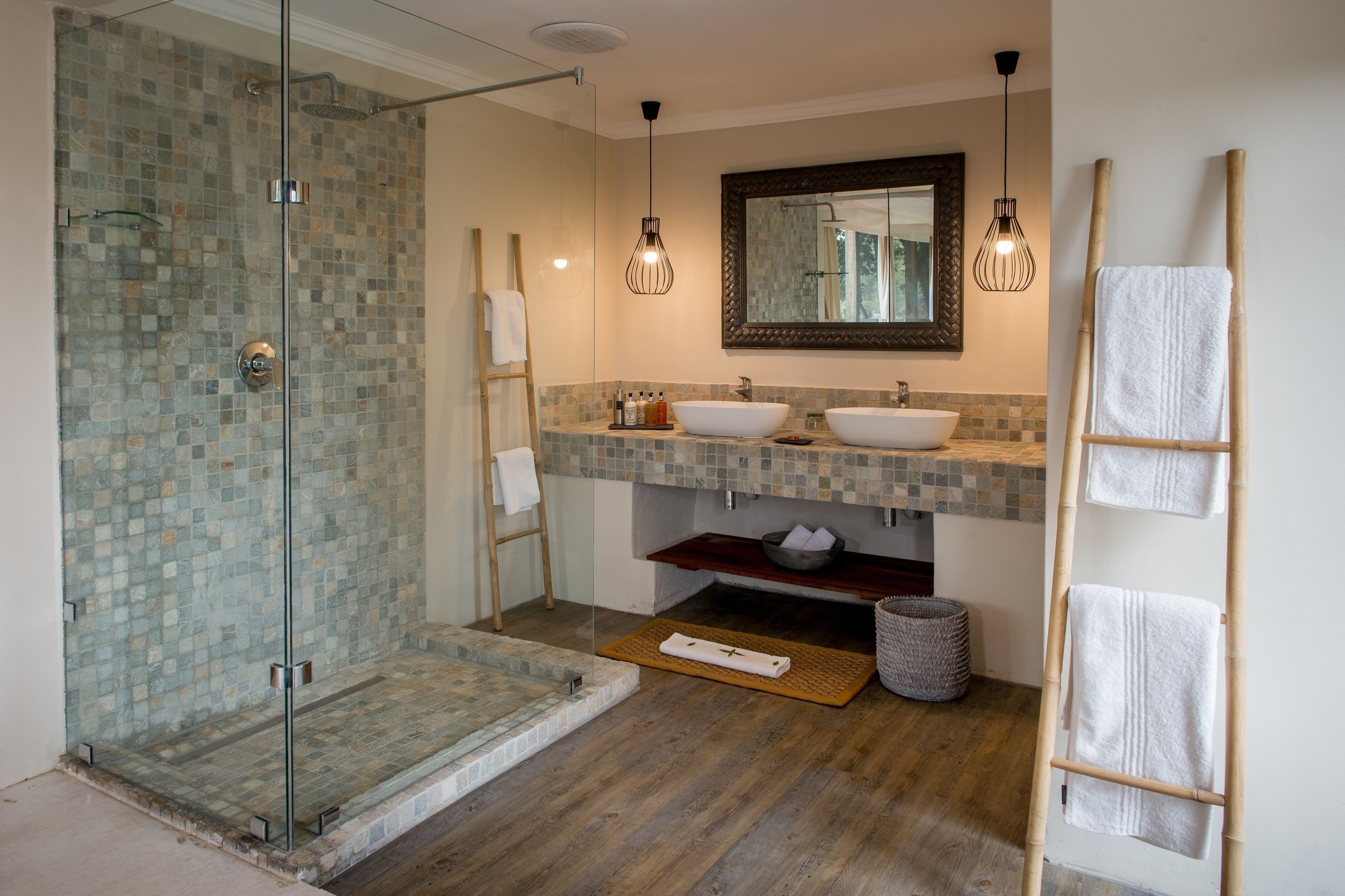 A bathroom with a glass-enclosed shower, two sinks, a large mirror, and hanging pendant lights.