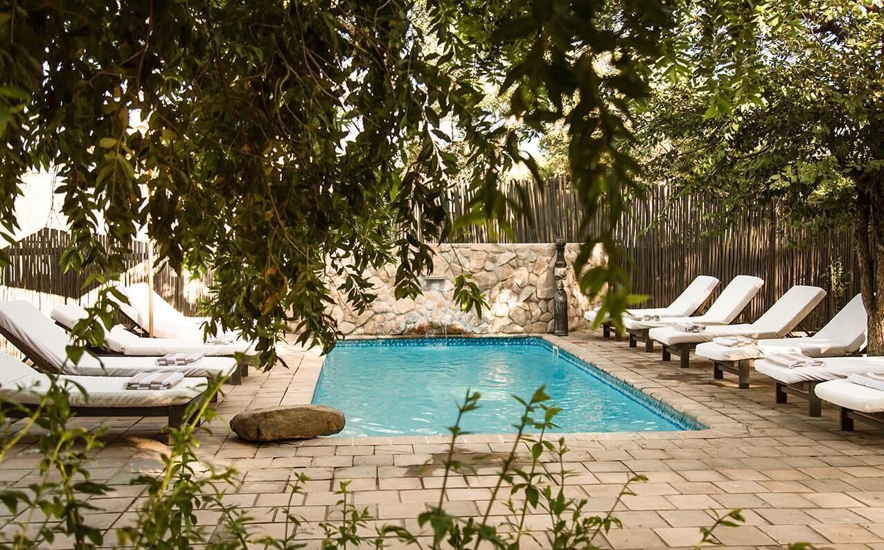 A rectangular pool with lounge chairs around it, surrounded by a stone wall and greenery.