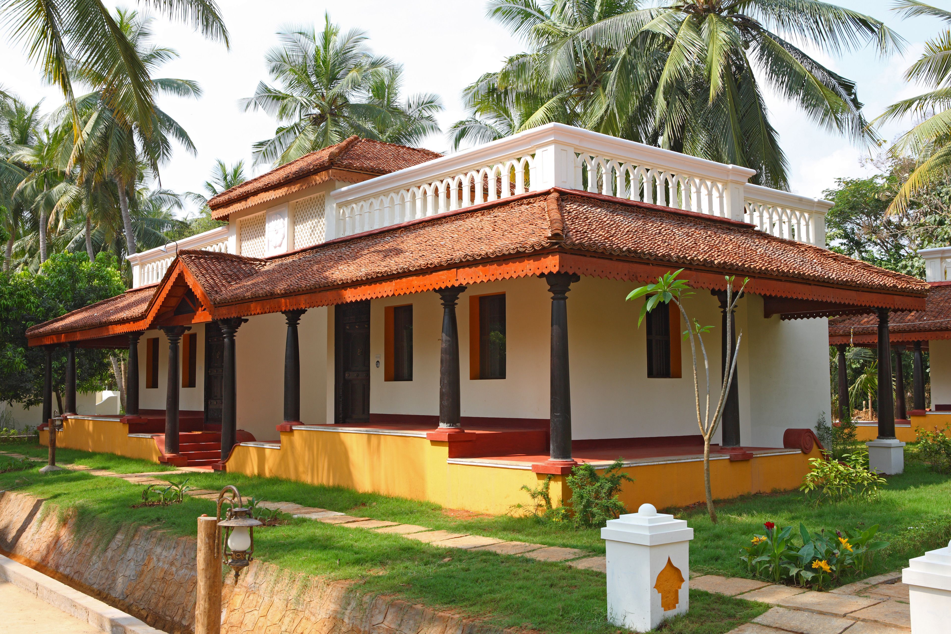 A traditional house with a tiled roof, a porch with columns, and a well-maintained garden with palm trees and flowers.