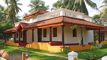 A traditional house with a tiled roof, a porch with columns, and a well-maintained garden with palm trees and flowers.