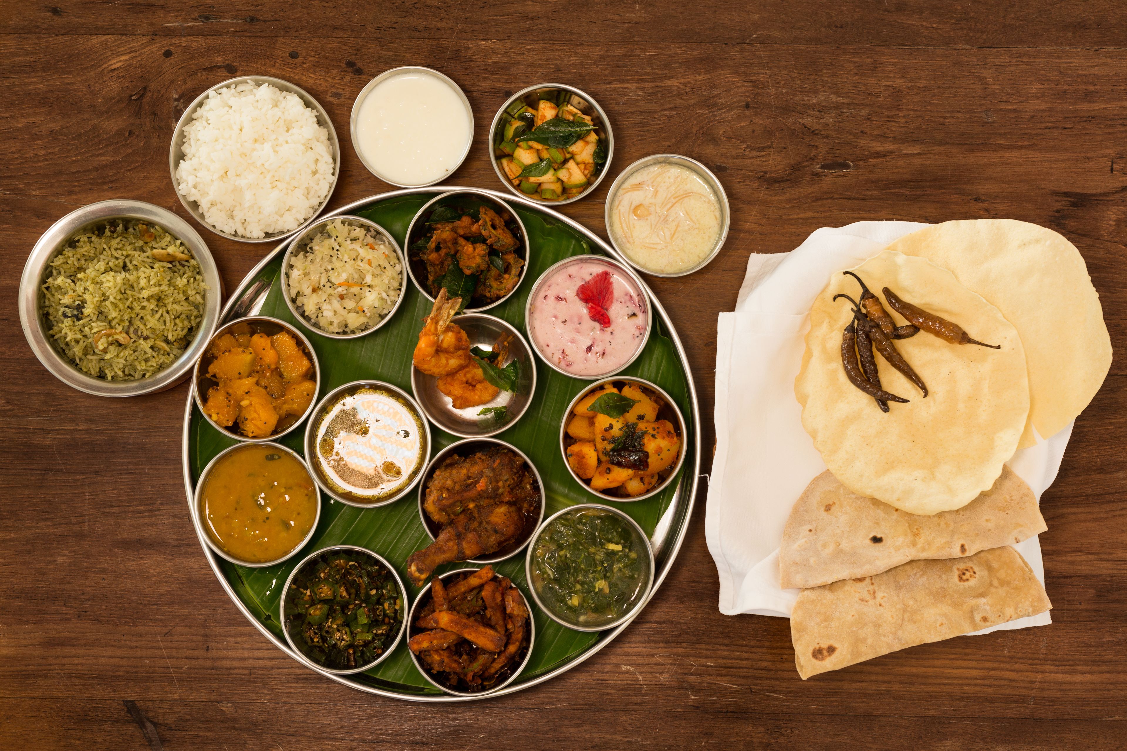 A variety of dishes arranged on a banana leaf and a plate, including rice, curries, and flatbreads.