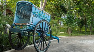 Un carruaje azul con diseños decorativos, estacionado sobre un sendero empedrado rodeado de vegetación.