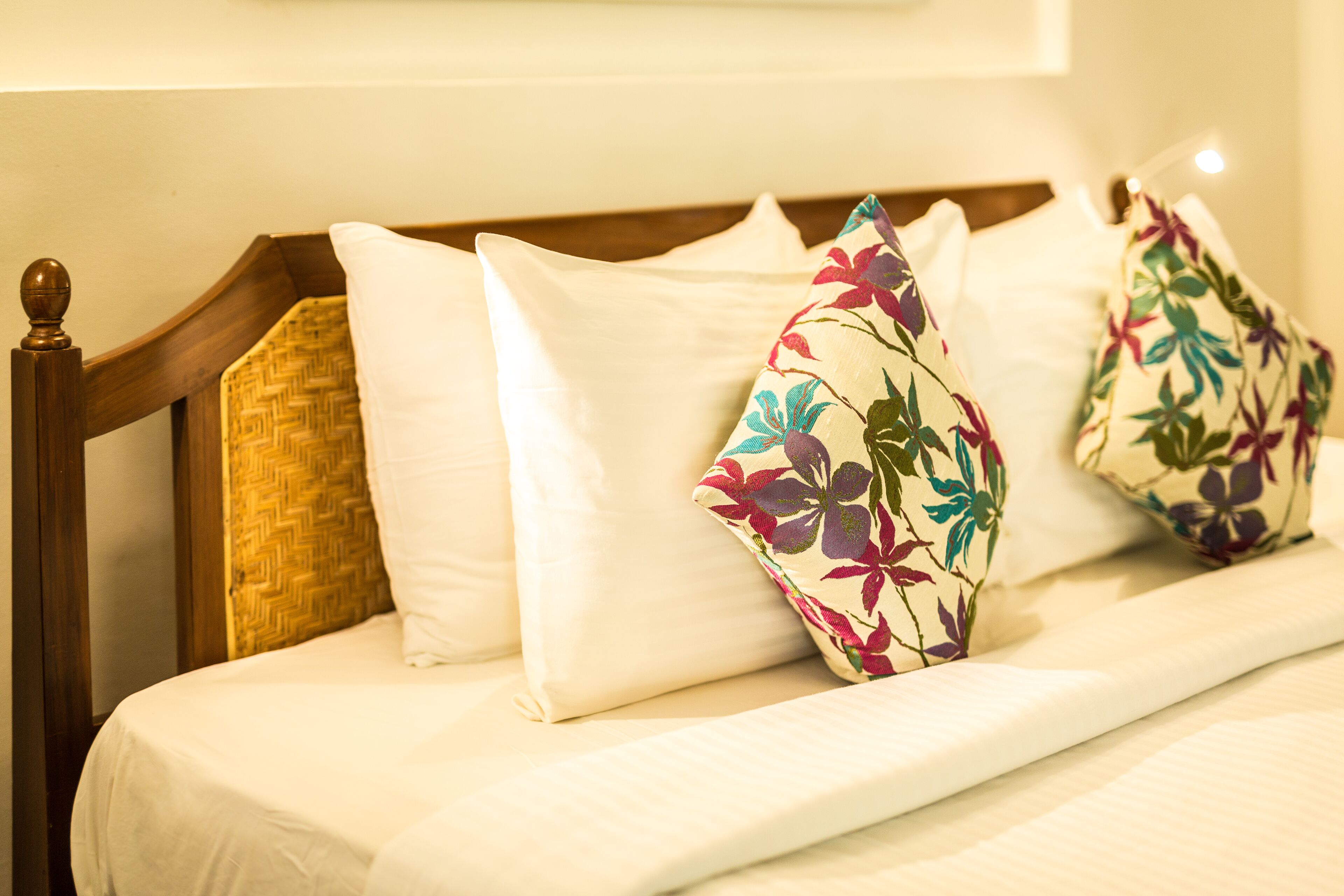 A bed with white bedding and floral-patterned pillows.