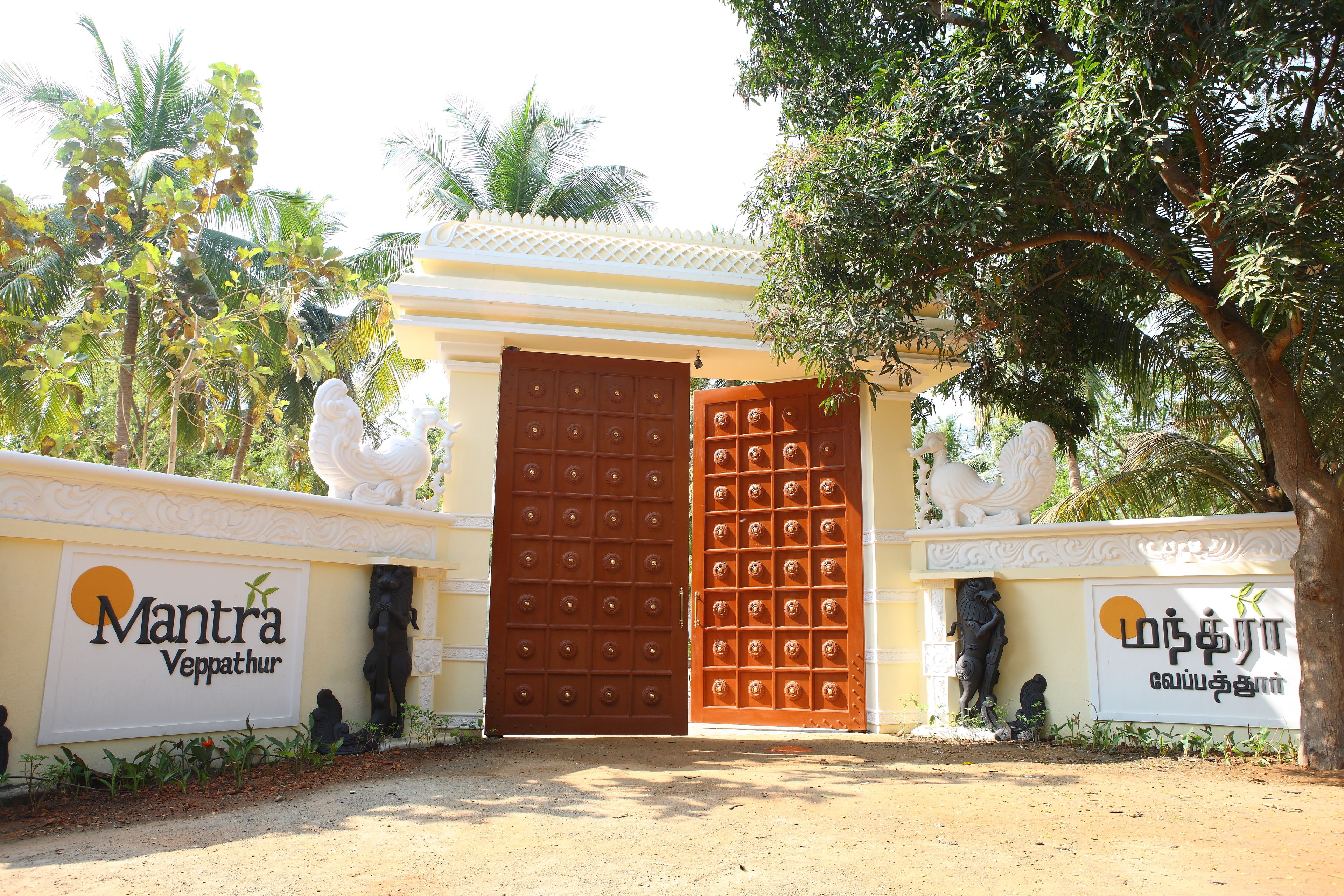 A gated entrance with a large brown door, two statues on either side, and signs with text.