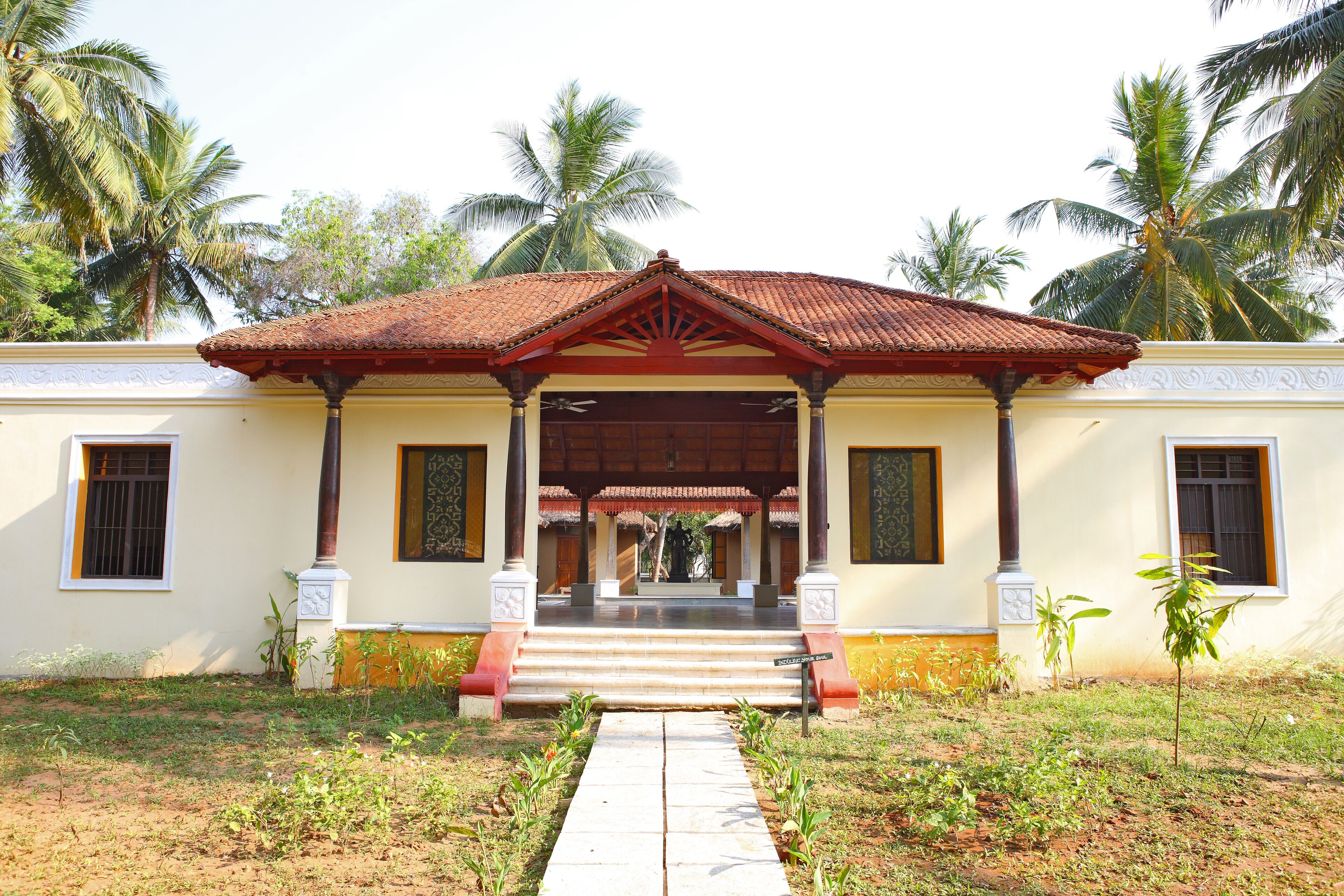 A building with a covered entrance, steps leading up to it, and palm trees in the background.