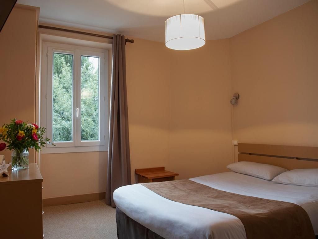 A bedroom with a bed, bedside table, lamp, window, and curtains.